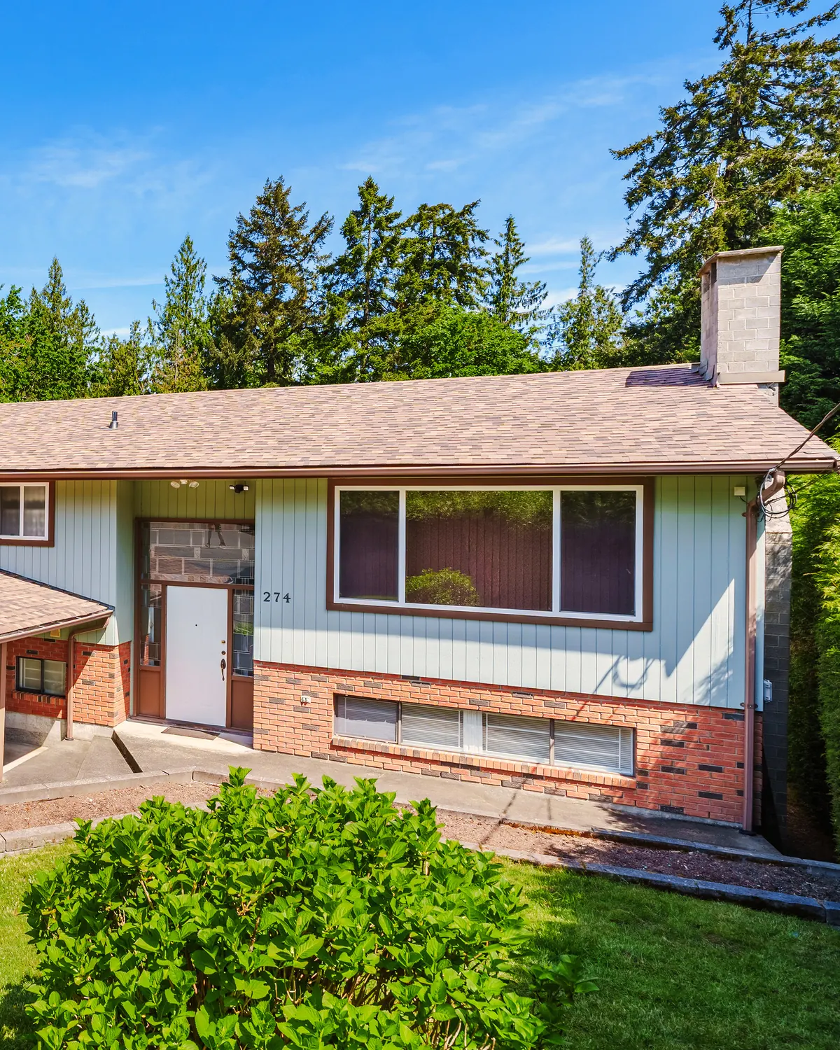 The front of 274 Emery Way, with a stone entry, a large picture window and shrubs out front
